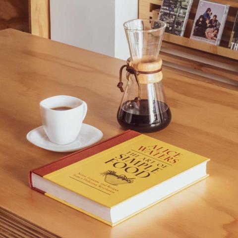 Imagen de una taza de café, un chemex y un libro.